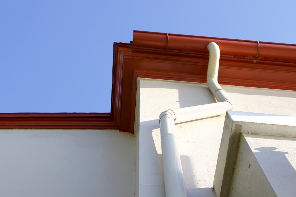 House roofline showing gutters and downpipe against blue sky